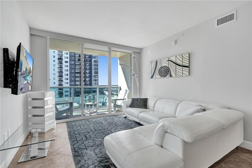 Modern condo living room with a white sectional sofa and balcony doors overlooking nearby high-rises.