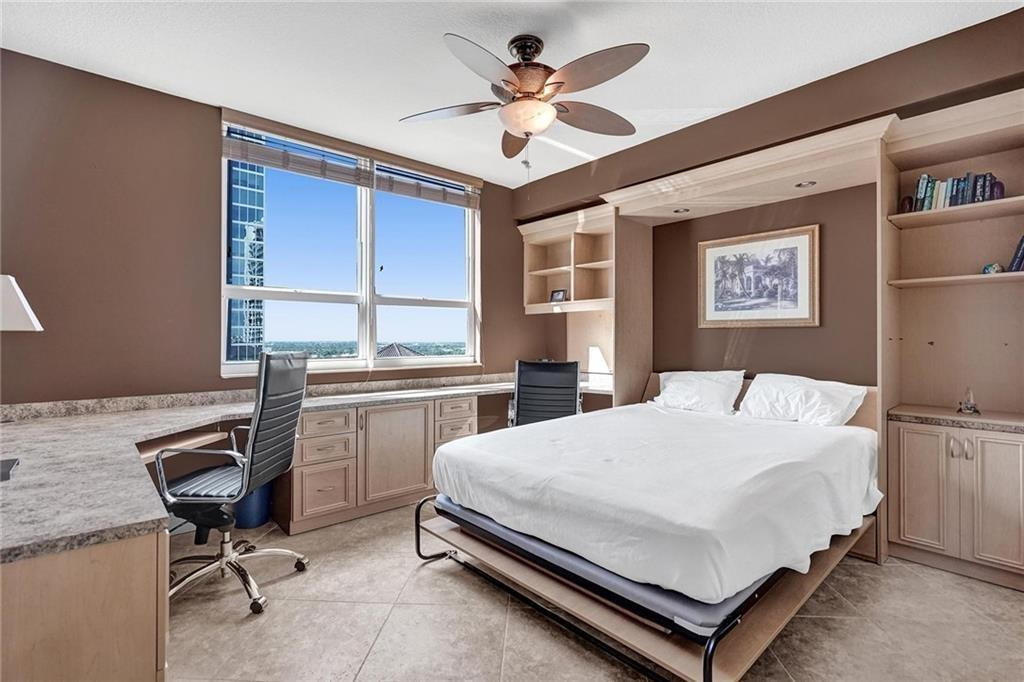 Bedroom with a white bed, built-in desk and cabinetry, and large windows overlooking water.
