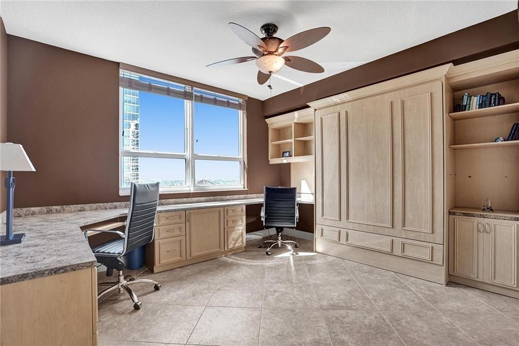 Home office with built-in desks and cabinetry, two chairs, and large windows.
