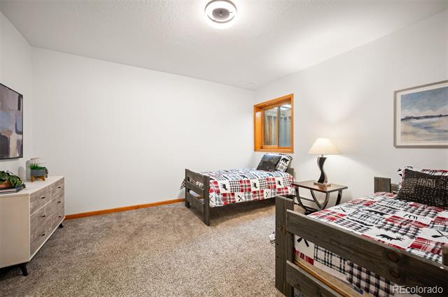 Bedroom with two wooden twin beds, plaid bedding, beige carpet, and a small wood-trimmed window.