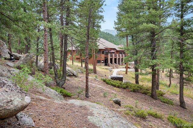 Multi-level home nestled among pine trees and rocky terrain, with a mountain ridge in the background.