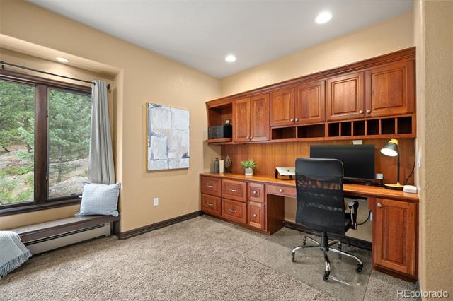 Home office with built-in wood cabinetry, a desk, and a window overlooking trees.