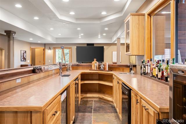 Indoor bar with U-shaped wood counters, a sink, bottles on display, and a wall-mounted television.
