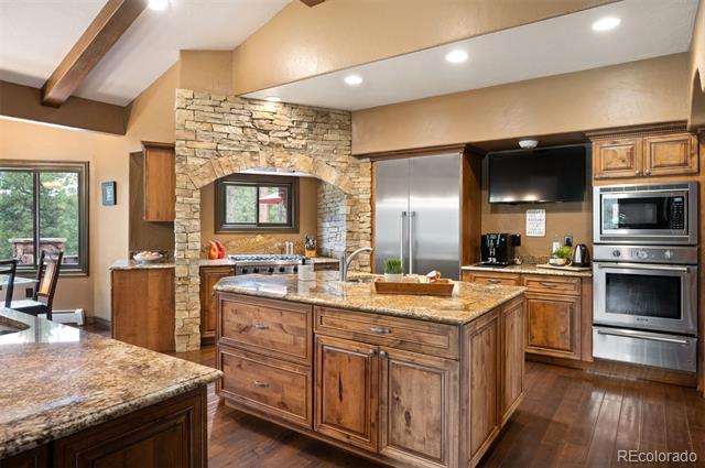 Kitchen with a granite island, rustic wood cabinetry, stainless steel appliances, and a stone cooktop arch.