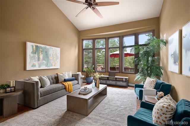 Staged living room with vaulted ceiling, large windows, gray sofa, and teal armchairs.