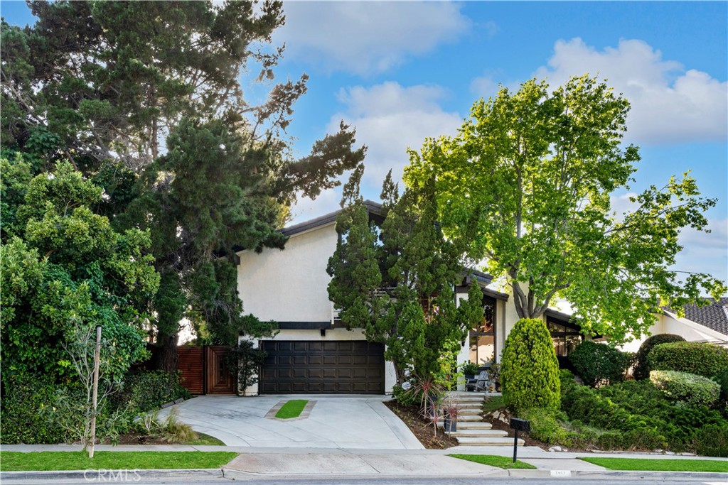 Two-story home with a dark garage door, wide driveway, mature trees, and landscaped front steps.