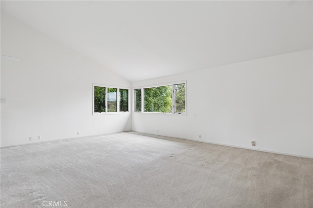 Vacant room with light carpet and corner windows overlooking greenery.