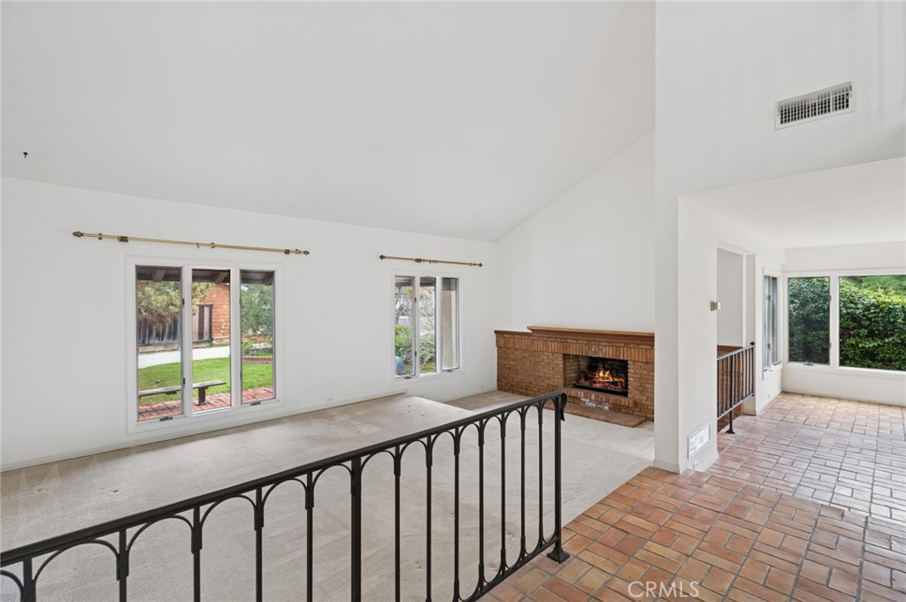 Vacant living room with a brick fireplace, garden-facing windows, and adjoining terracotta-tiled area.
