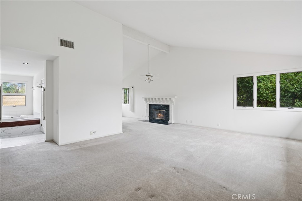 Vacant living room with a fireplace, large window, and adjoining bathroom tub.