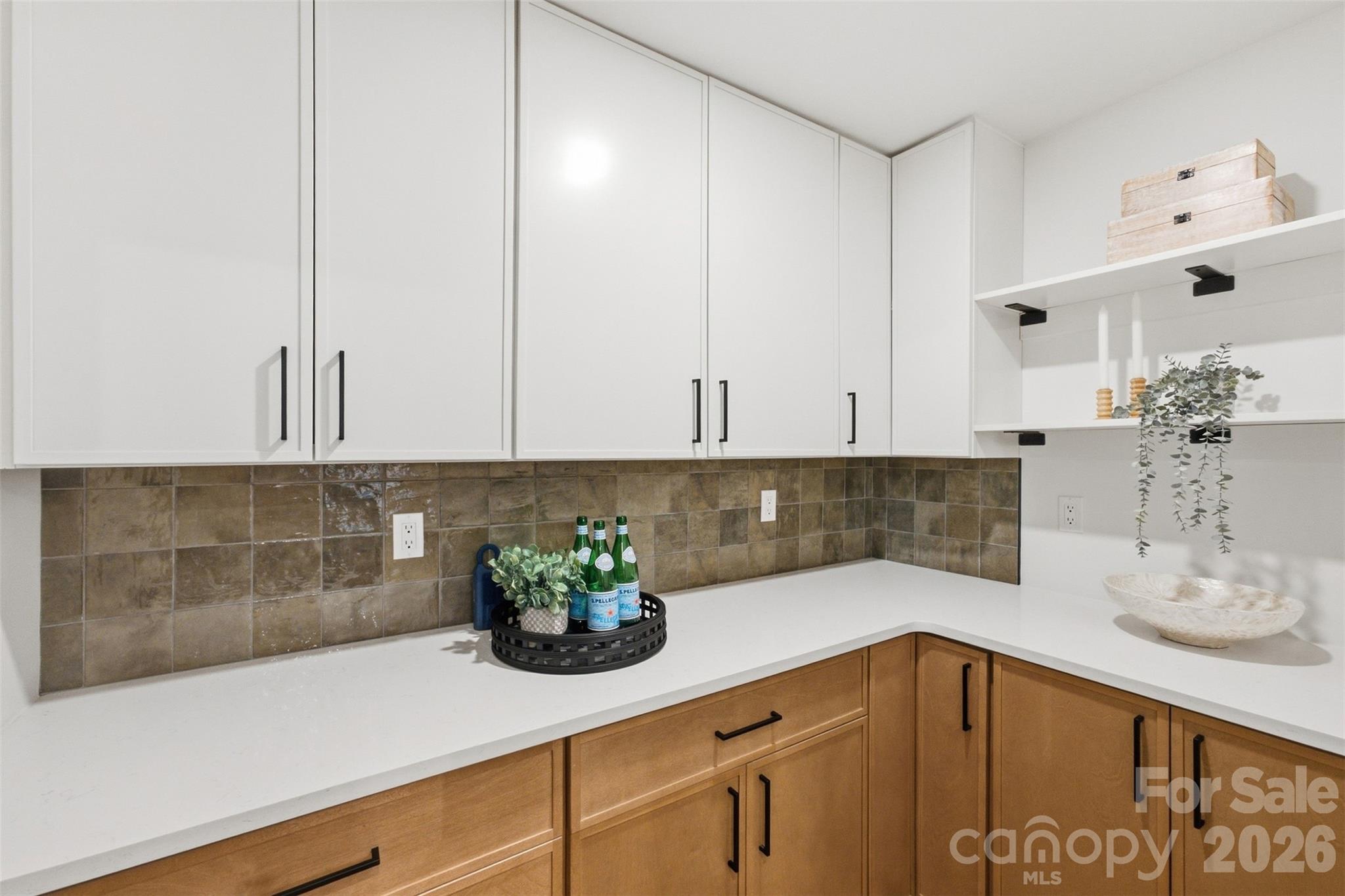 Kitchen with white upper cabinets, warm wood lower cabinets, and a brown tile backsplash.