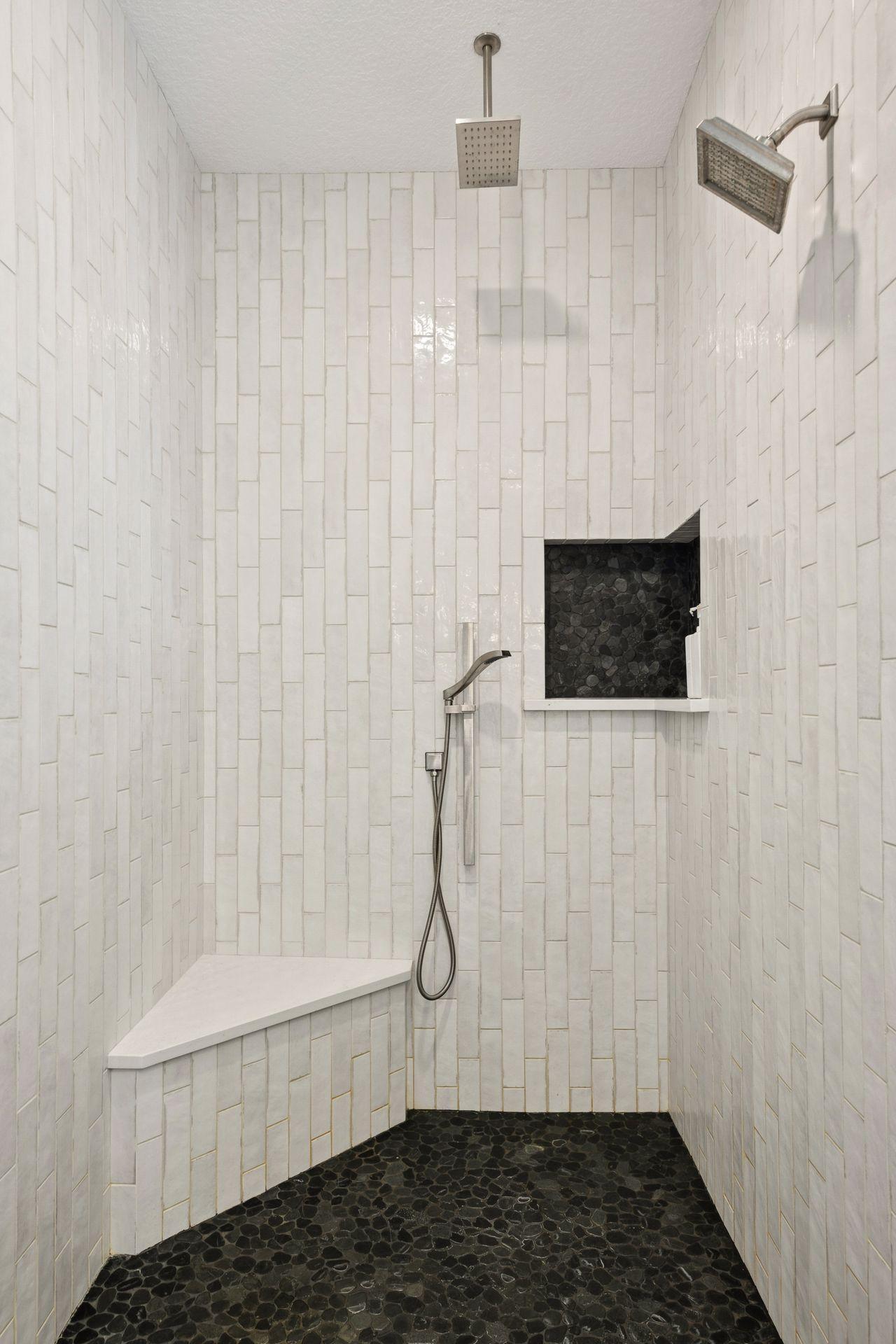 Walk-in shower with white tile, dark pebble flooring, a built-in bench and recessed niche.