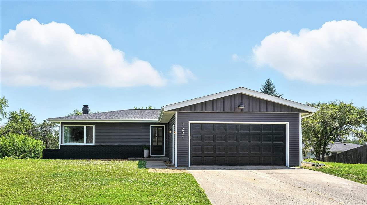 Single-story gray house with a wide black garage door and concrete driveway.