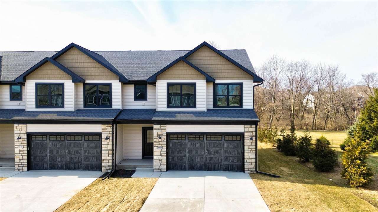 Paired townhouse-style homes with stone-accented façades, dark garage doors, and a shared roofline.