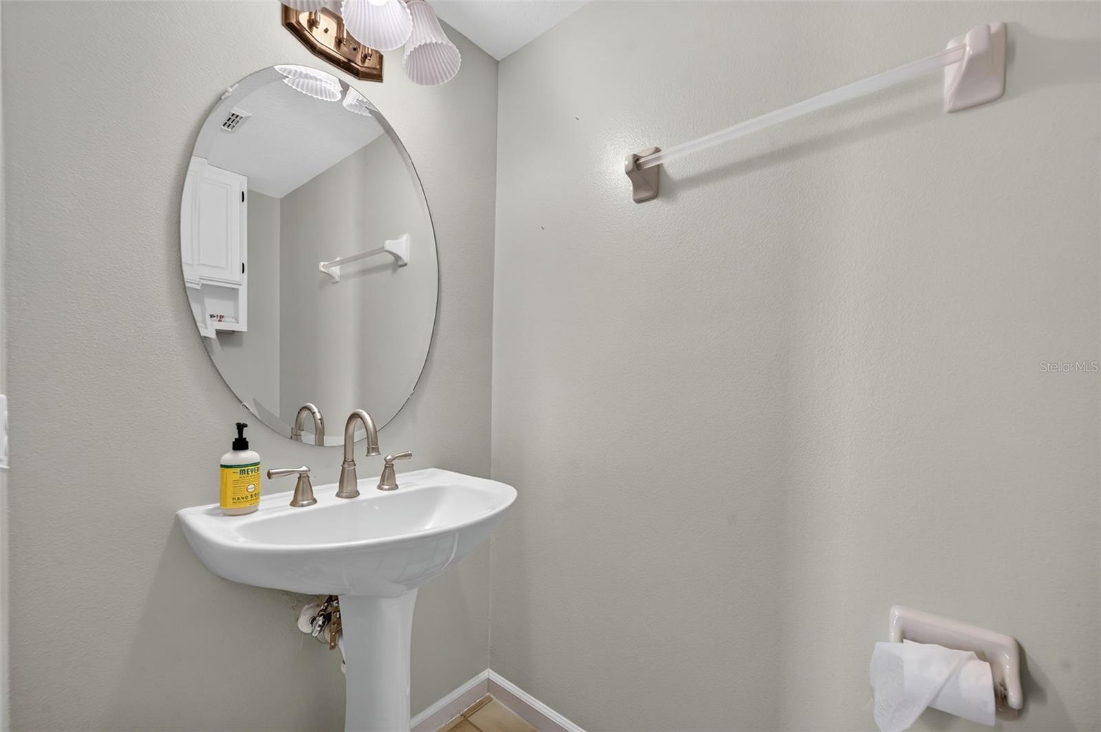 Bathroom pedestal sink with an oval mirror and wall-mounted towel bar.