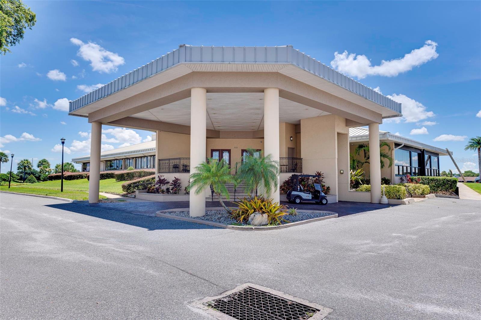 Clubhouse exterior with a columned entrance canopy, glass-sided wings, and a golf cart.