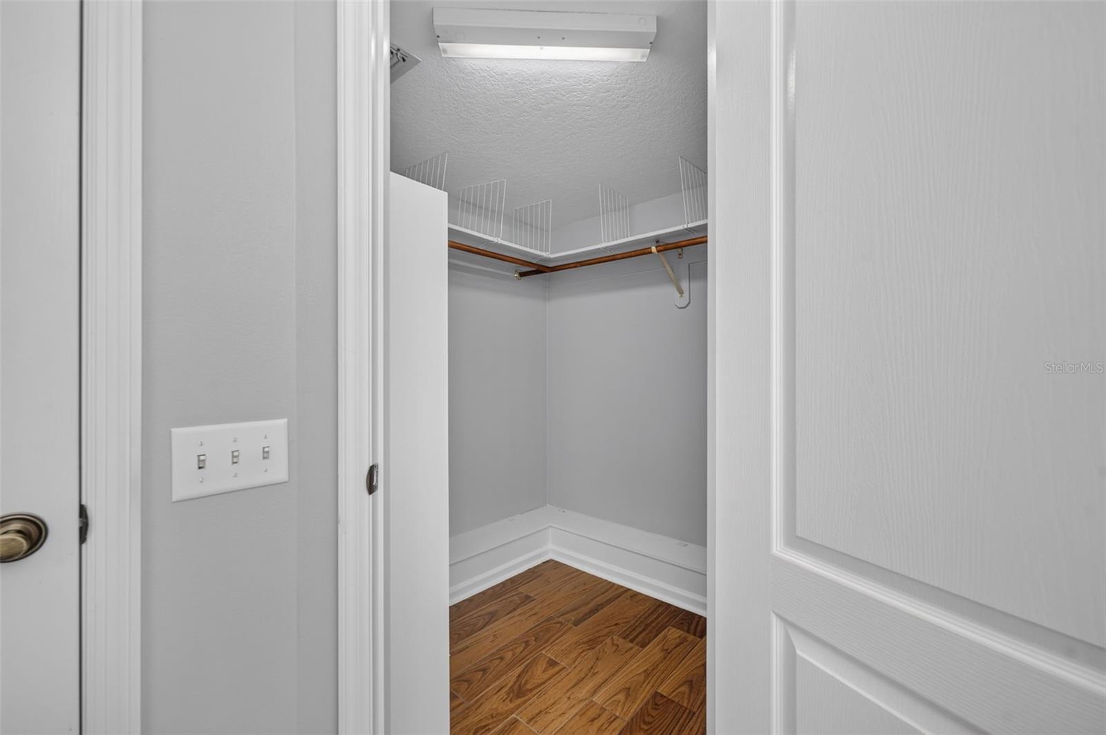 Walk-in closet with wire shelving, a wooden hanging rod, and hardwood flooring.