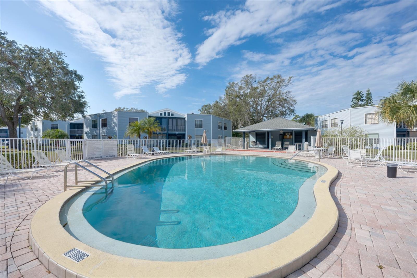 Outdoor swimming pool with curved steps, lounge chairs, and blue apartment buildings.