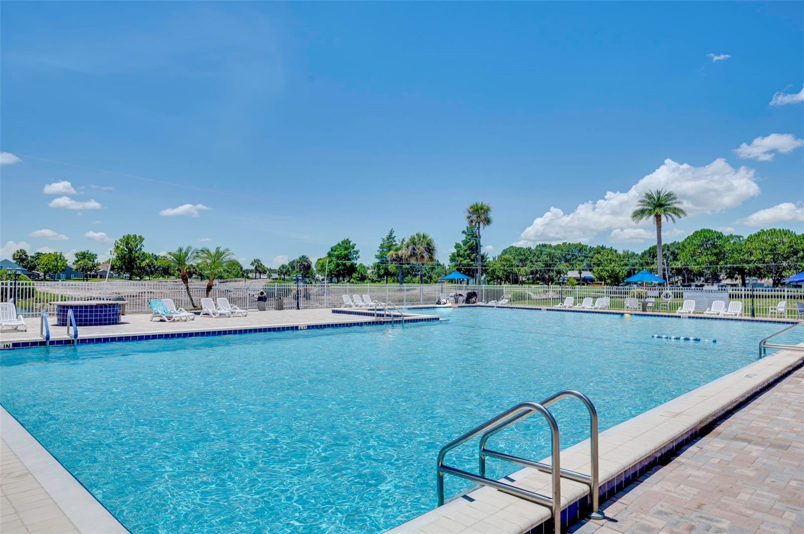 Outdoor community pool with a tiled deck, lounge chairs, and palm trees.
