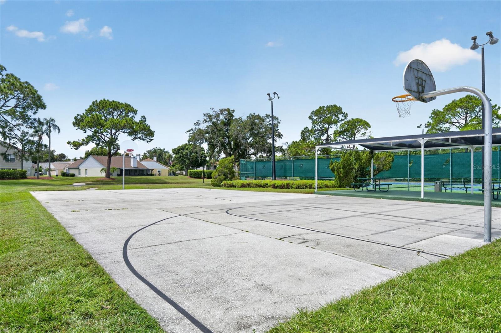 Community basketball court with a hoop, fenced tennis courts, and picnic tables.