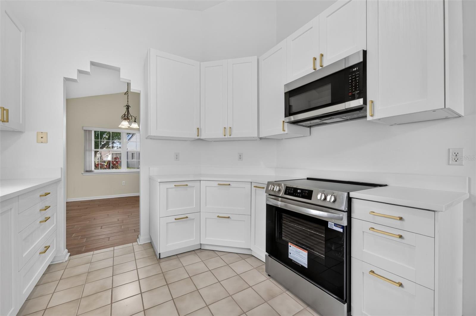 Kitchen with white cabinets, brass hardware, stainless-steel appliances, and a tiled floor.
