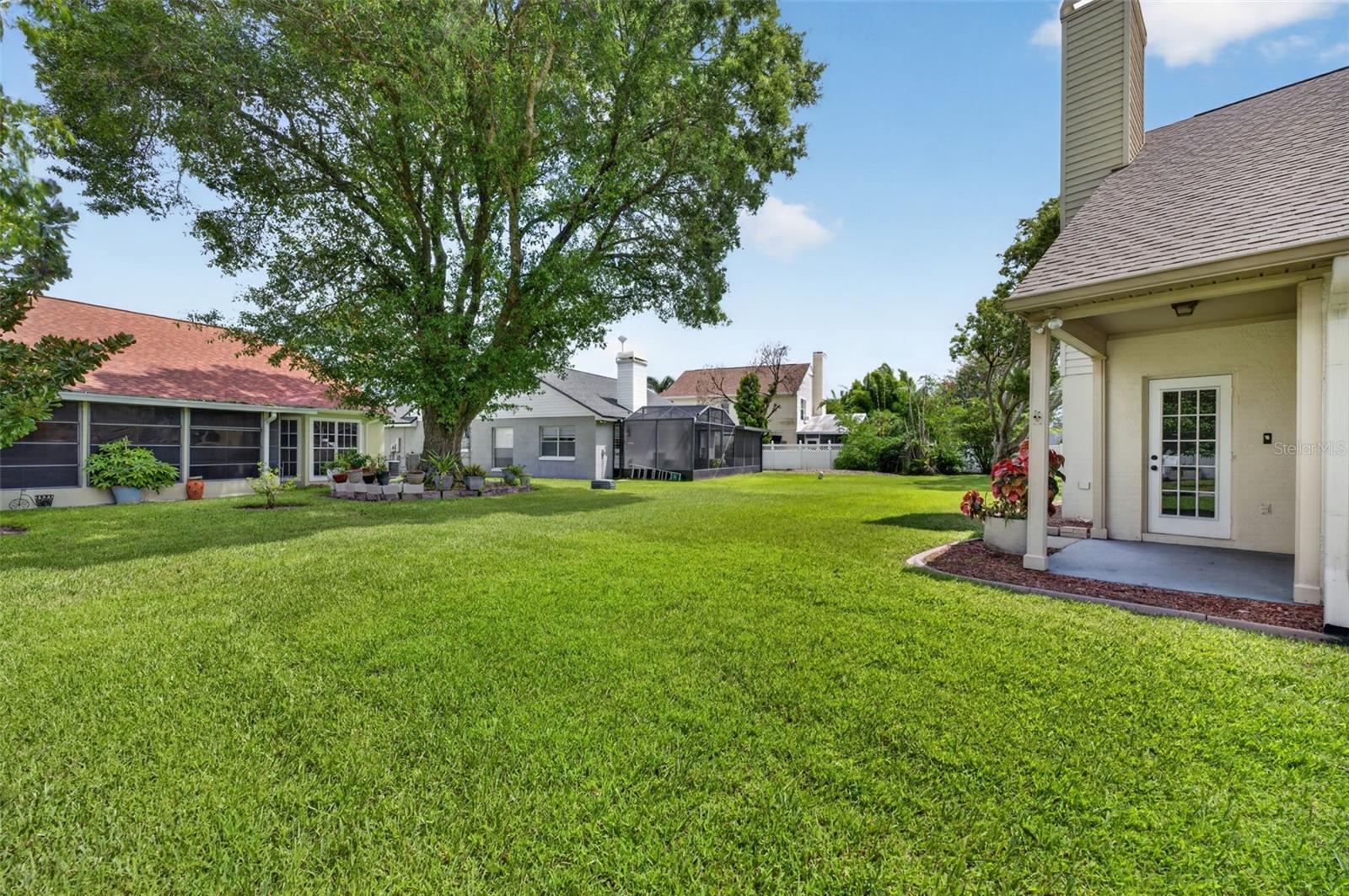 Backyard with a broad green lawn, mature shade tree, screened patio enclosure, and covered porch.