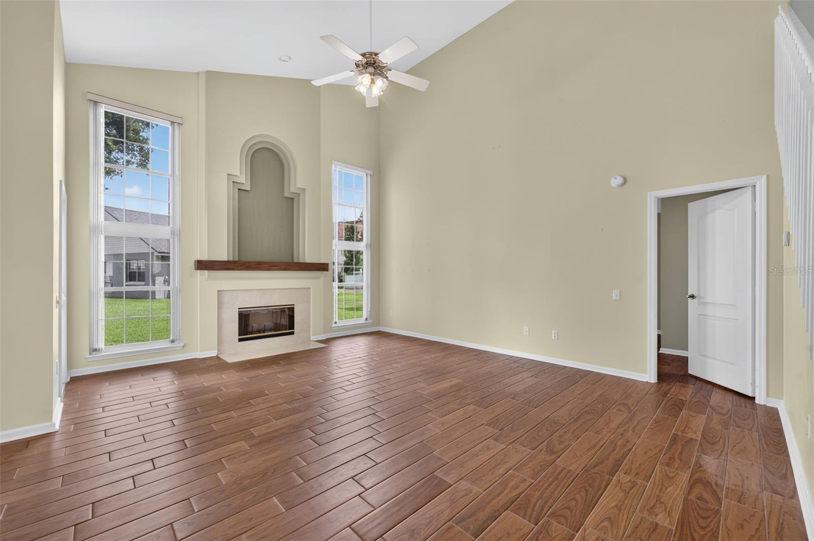 Vacant living room with an arched fireplace, tall windows, and wood-look tile flooring.