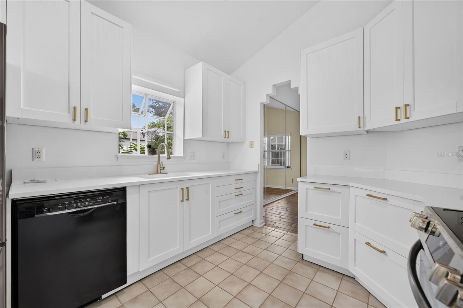 Bright kitchen with white shaker cabinets, brass hardware, tiled floors, and a window above the sink.
