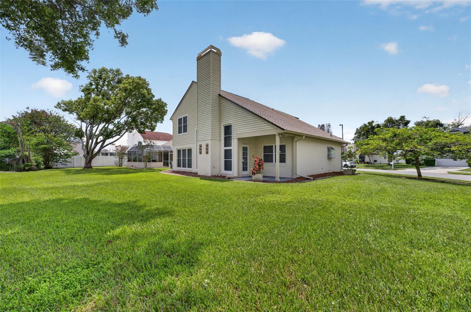House exterior with a tall chimney, covered patio, and broad green lawn.