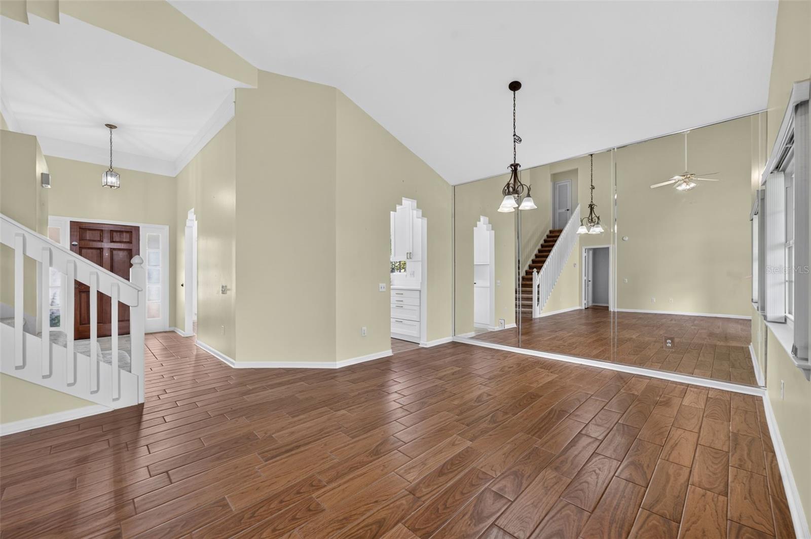 Empty living room with vaulted ceiling, wood-look tile floors, staircase, and mirrored wall.