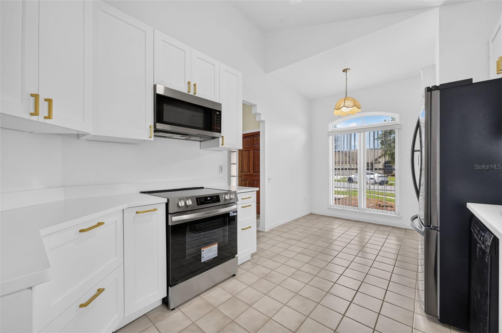 Bright kitchen with white cabinets, stainless-steel appliances, and a window with vertical blinds.