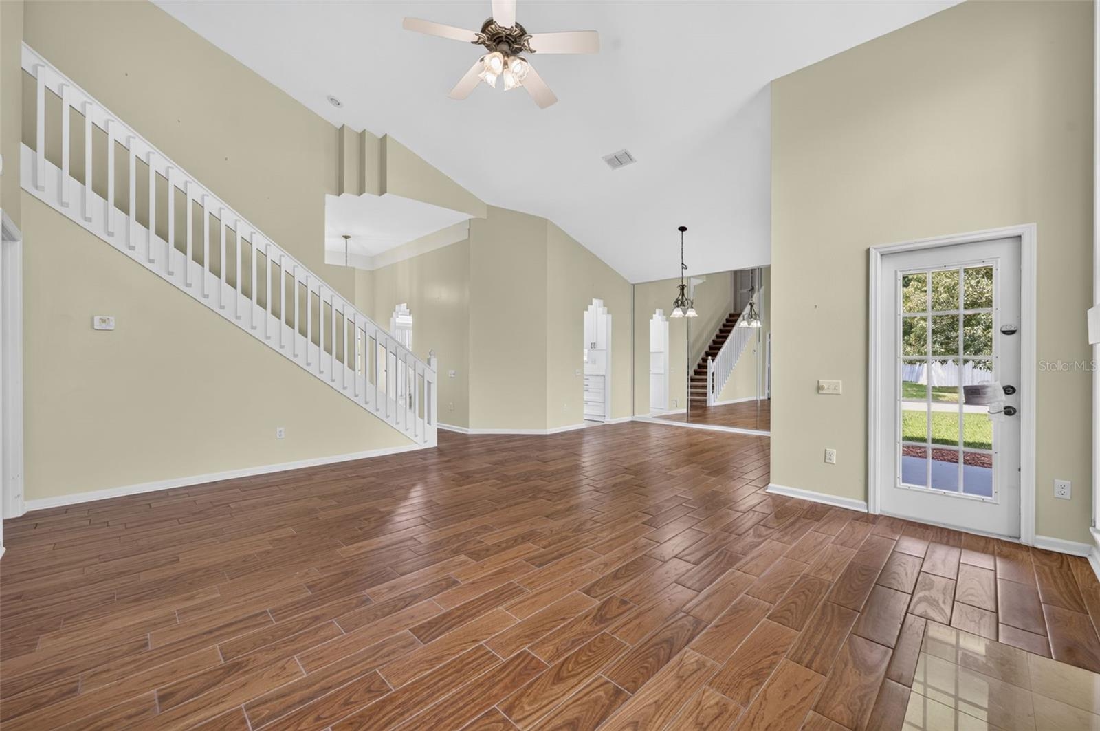 Open living room with wood-look tile floors, a white-railed staircase, and a glass-paneled door.