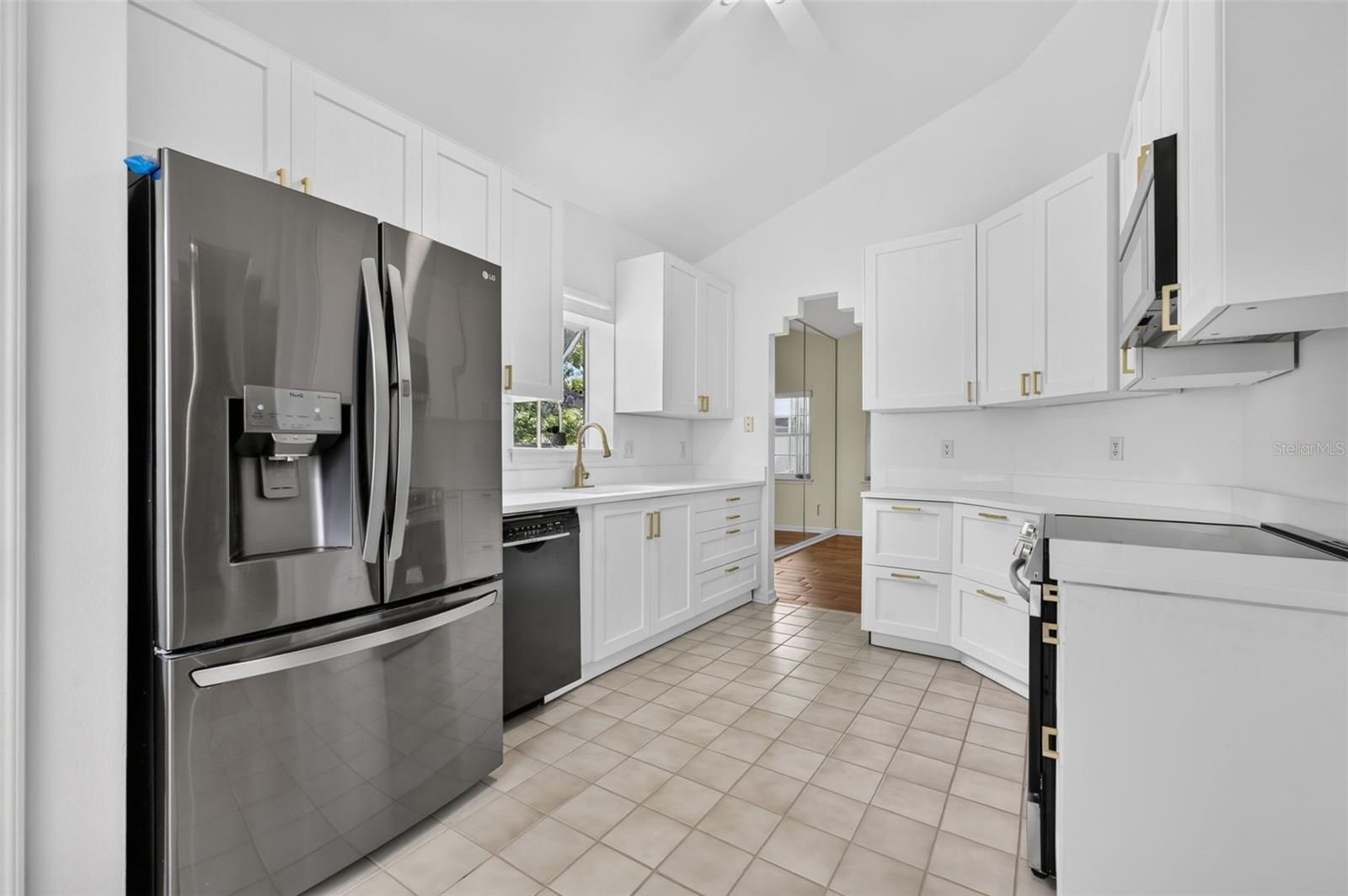 White kitchen with stainless steel appliances, gold-tone cabinet hardware, and a window above the sink.
