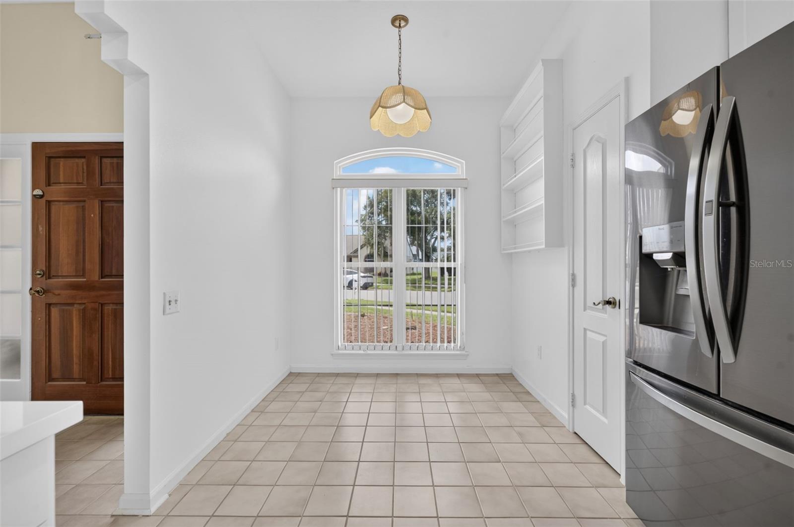 Unfurnished breakfast nook with tiled floors, an arched window, built-in shelves, and a stainless-steel refrigerator.