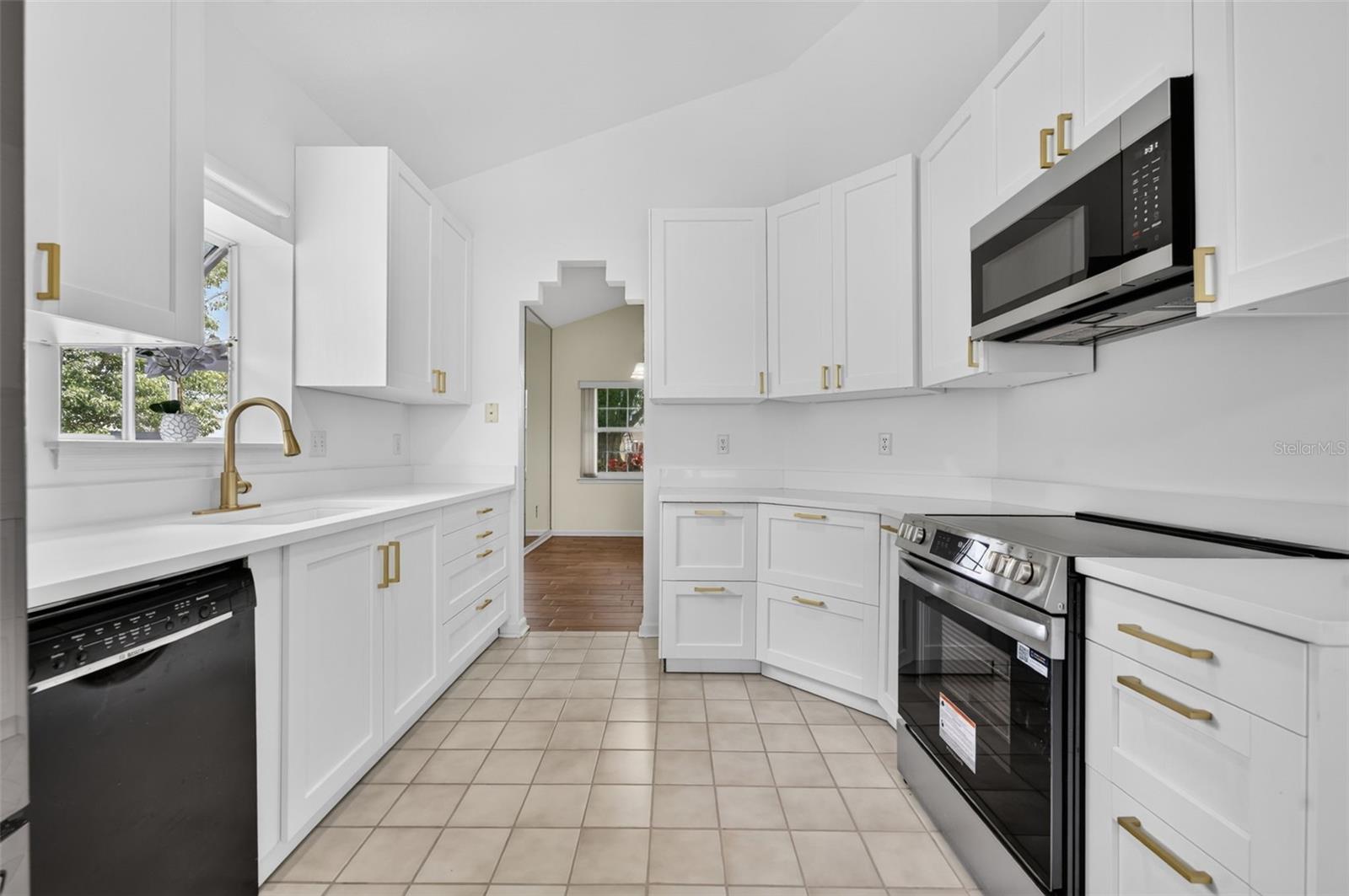 Bright white kitchen with gold fixtures, tiled floor, and stainless steel range.