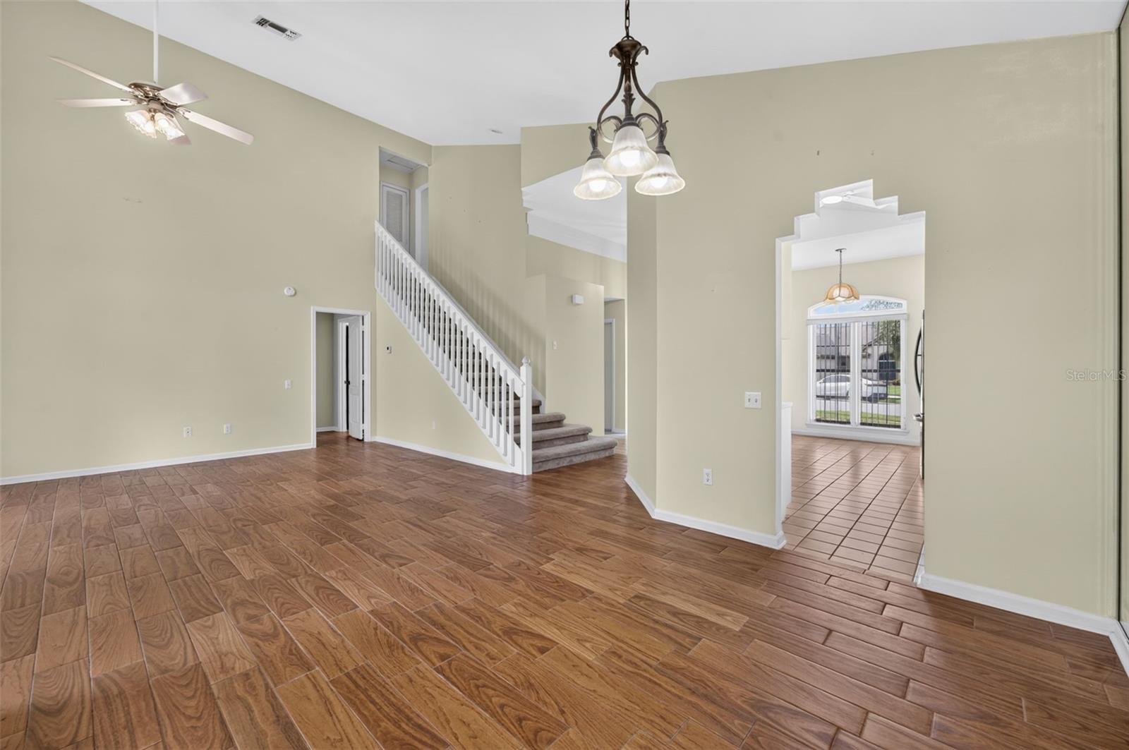 Vacant living area with wood-look tile floors, a white staircase, and adjoining tiled dining room.