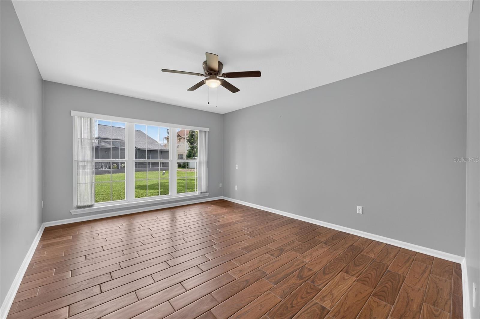 Empty room with wood-look tile flooring, gray walls, and a wide window overlooking a grassy yard.