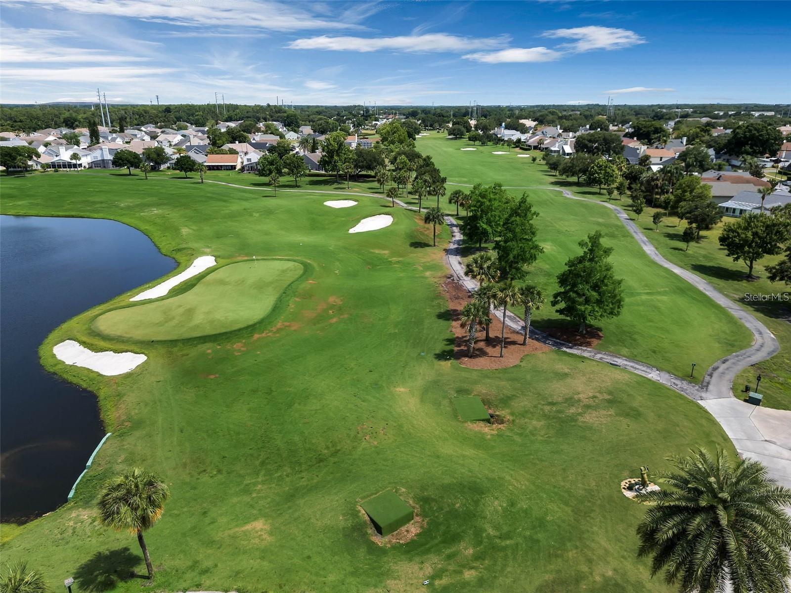 Aerial golf course with a pond, sand bunkers, cart paths, and homes along the fairways.