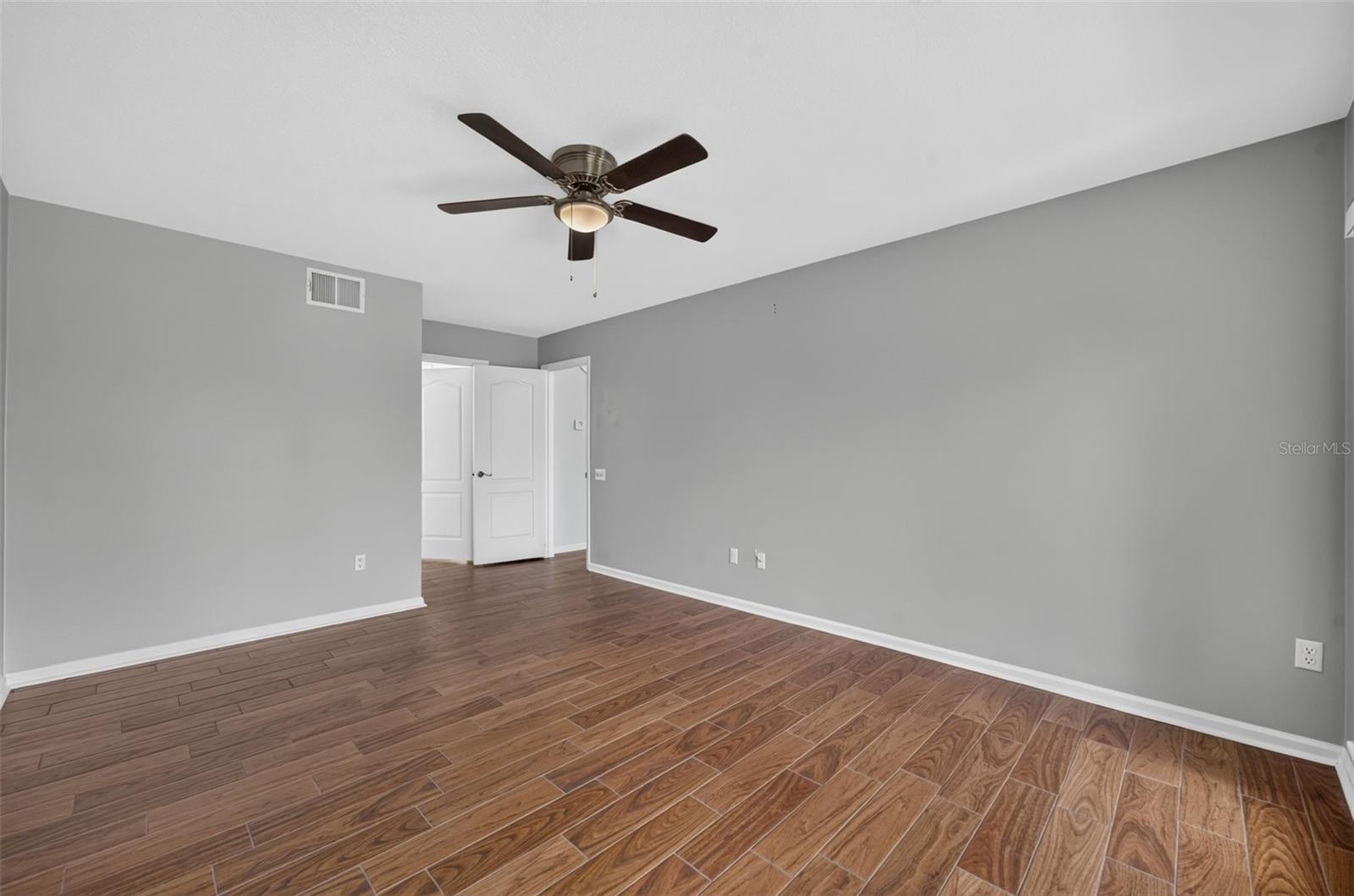 Empty room with gray walls, wood-look tile flooring, and a ceiling fan with light.