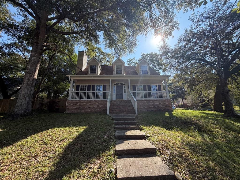 Two-story house with a covered porch and three dormers beneath mature shade trees.