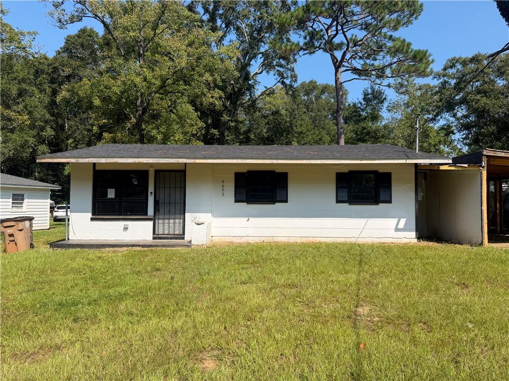 Single-story white house with a covered carport, broad lawn, and mature trees behind it.