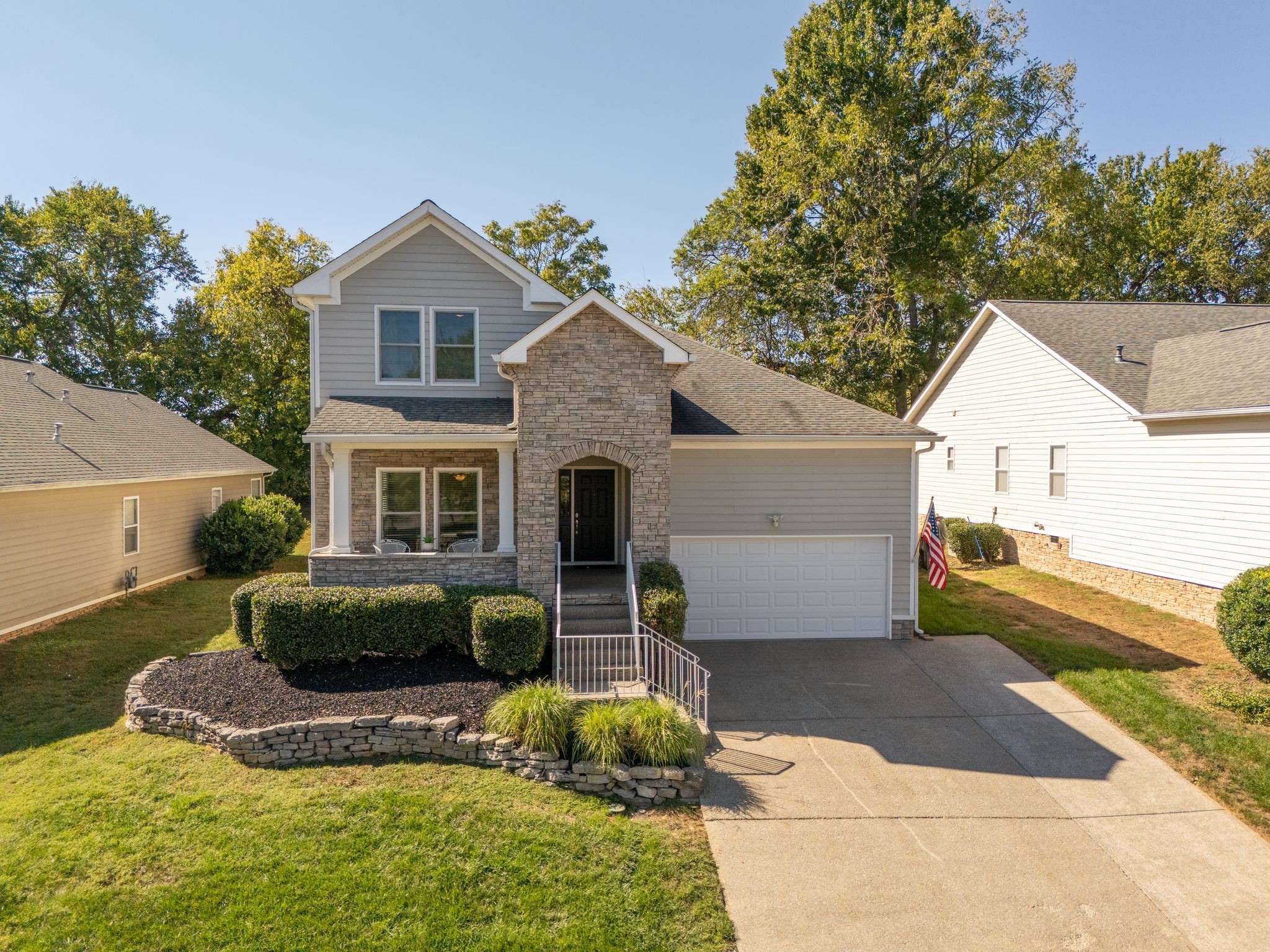 Two-story gray house with a stone entry, attached garage, and landscaped front yard.