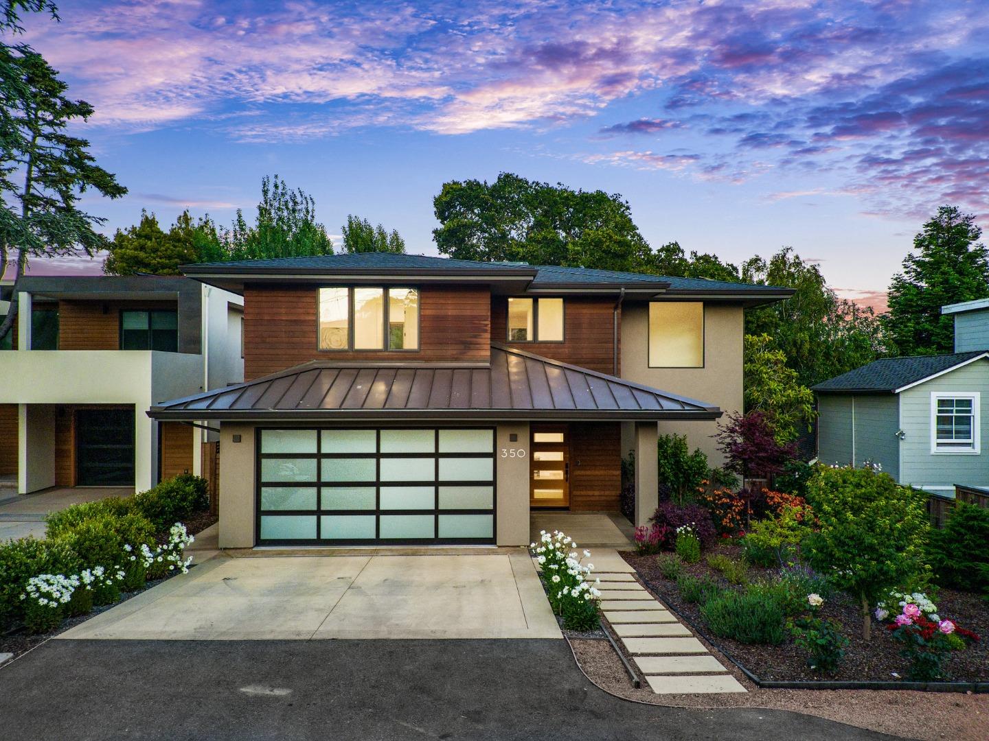 Modern two-story home with wood siding, a broad garage, and landscaped gardens at dusk.