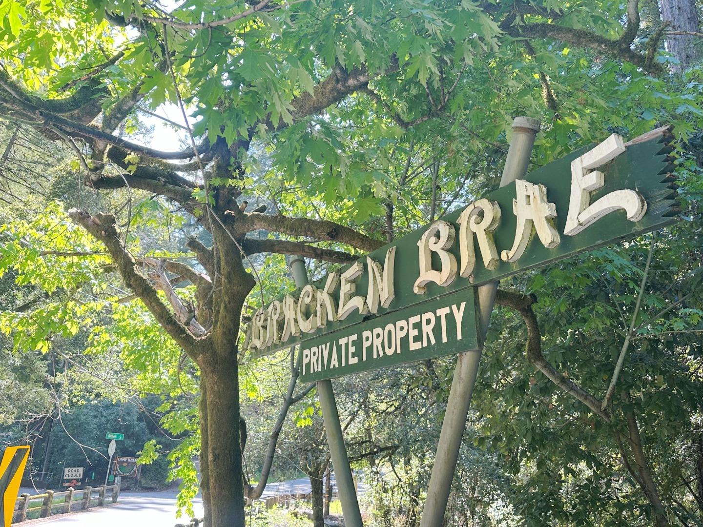 Boulder Creek sign with a Private Property notice beneath leafy trees beside a road.