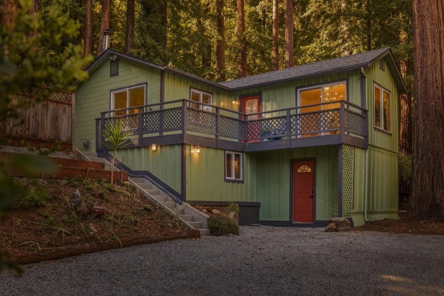 Green home with a raised wraparound deck among redwood trees, photographed at golden hour.