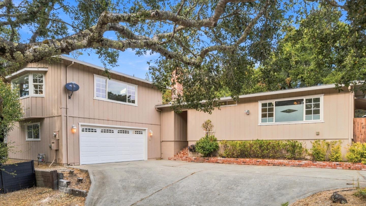 Tan split-level home with an attached two-car garage beneath sprawling oak branches.