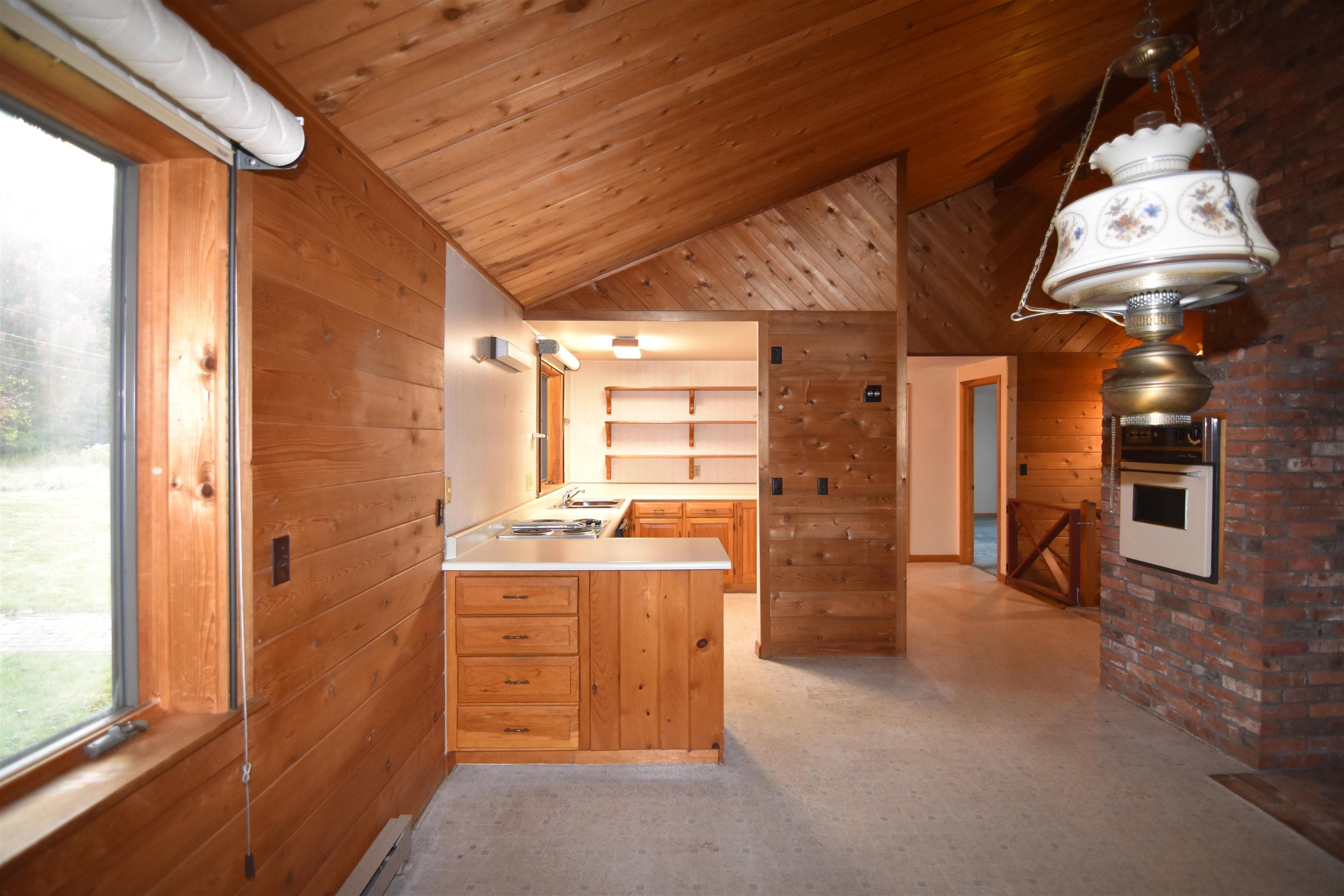 Vacant wood-paneled kitchen with a vaulted ceiling, built-in shelves, and brick fireplace wall.