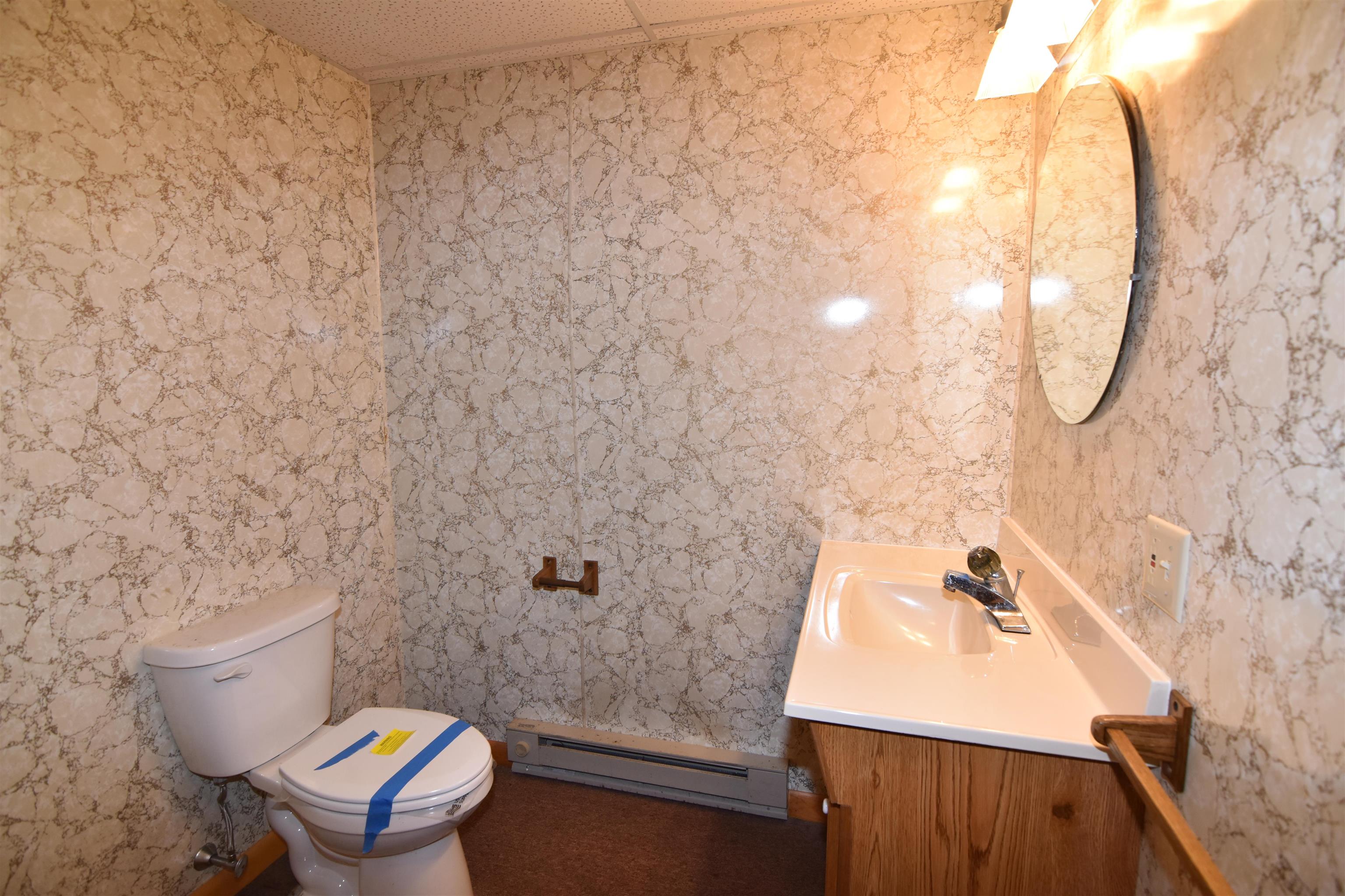 Bathroom with marble-pattern walls, a taped toilet, and a wood-front vanity with sink.