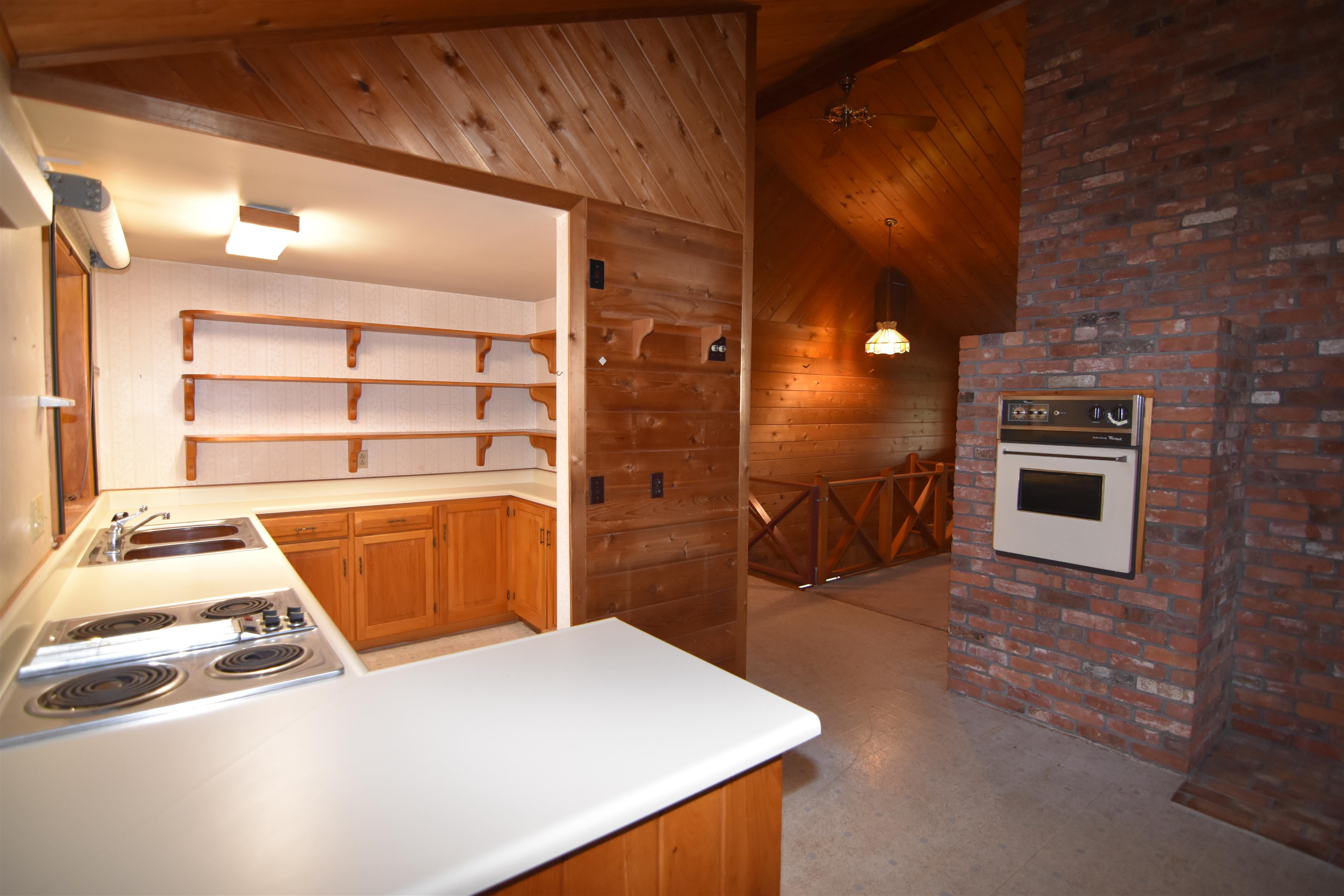Kitchen with wood cabinetry, open shelves, and a brick chimney wall with a built-in oven.