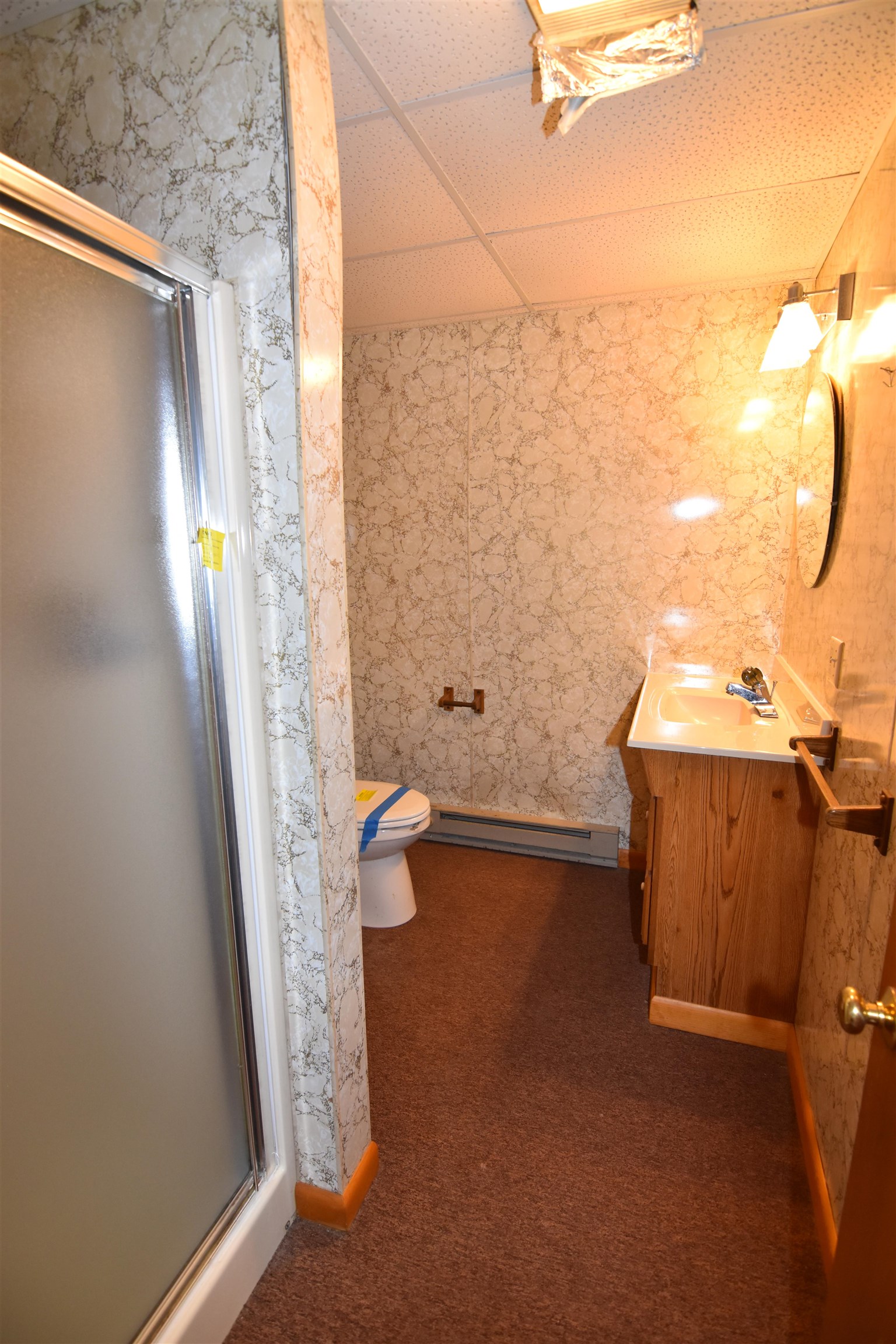 Bathroom with a frosted-glass shower, marble-pattern walls, and a wood vanity beside the toilet.
