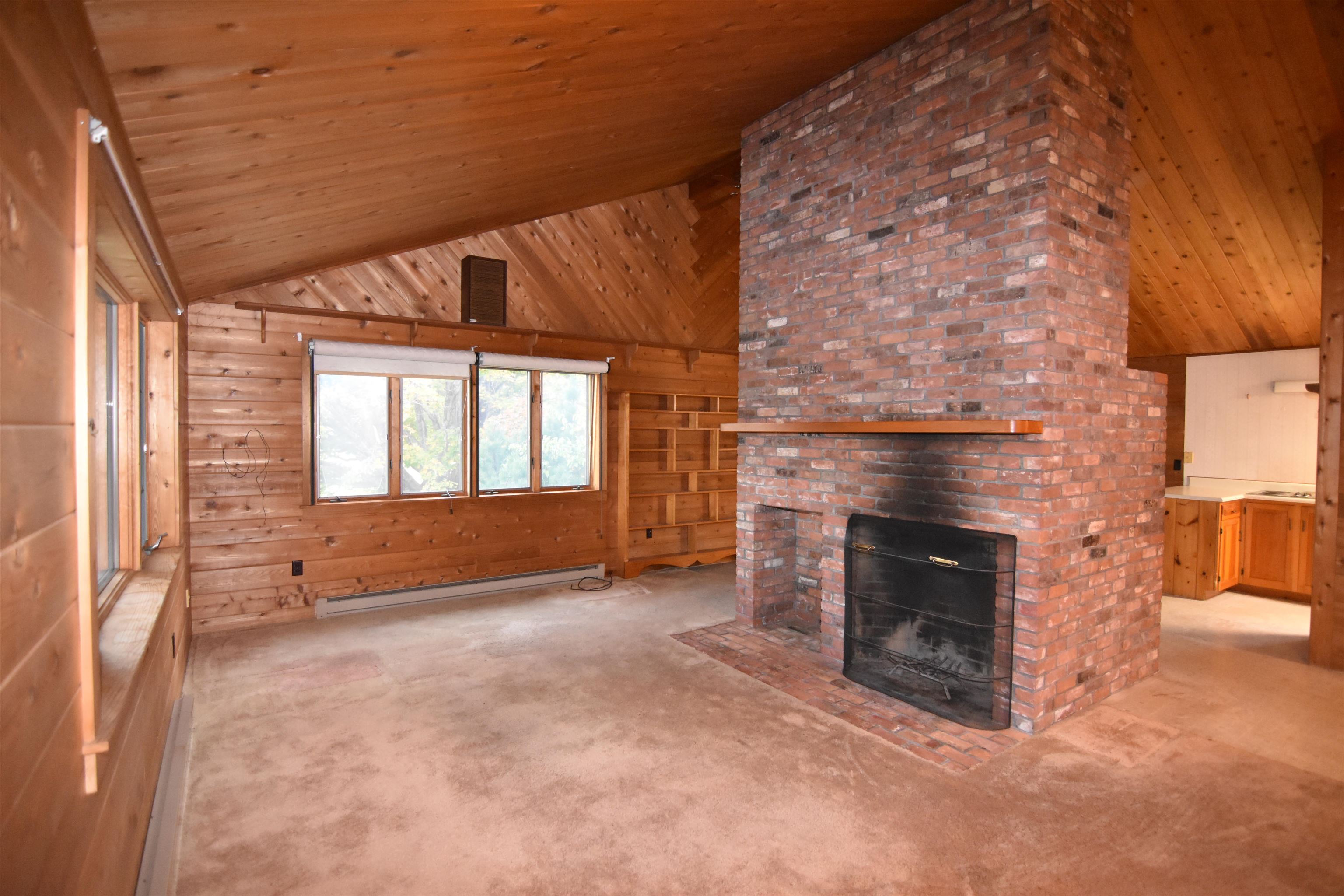 Living room with a vaulted wood ceiling, built-in shelves, and a large brick fireplace.